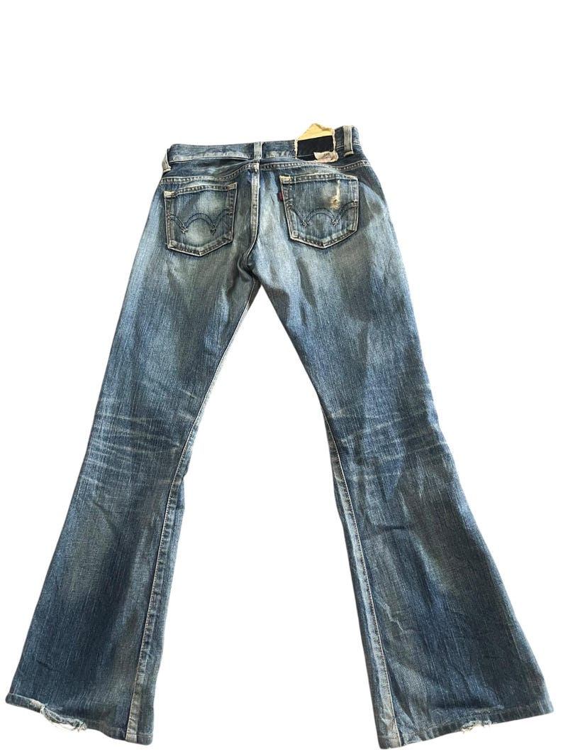 May include: Faded blue denim jeans with a flared leg design. The jeans feature classic five-pocket styling, a distressed look, and a leather patch on the back. The jeans are a vintage style.