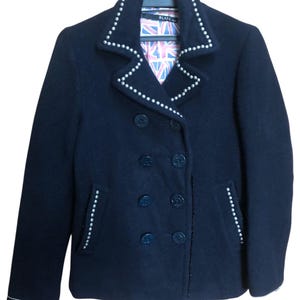 May include: A navy blue double-breasted coat with pearl-like studs along the collar and edges. The coat has a Union Jack patterned lining and four dark blue buttons on each side. The coat is hanging on a black hanger.