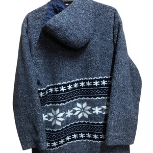 May include: A blue hooded sweater with a snowflake pattern on the lower back. The sweater is hanging on a black hanger. The snowflake design is white and navy blue.