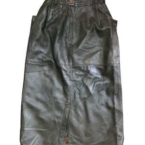 May include: A dark green leather skirt with a high waist and a button closure. The skirt has a knee-length hemline and a slit in the back. The leather appears to be slightly distressed.