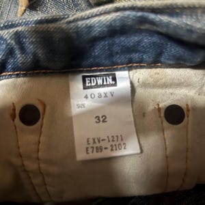 K&ouml;nnte beinhalten: Nahaufnahme der Innenseite einer blauen Jeans. Das Etikett lautet "EDWIN" und enth&auml;lt die Nummern "403XV", "32", "EXV-1271" und "E789-2102". Die Jeans weist Gebrauchsspuren auf.