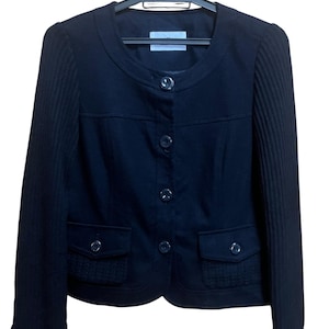 May include: A black jacket with a round neckline and button closure. The jacket has two front pockets and ribbed sleeves. It is hanging on a black hanger.