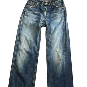 May include: Faded blue denim jeans with a button fly and classic five-pocket design. The jeans show signs of wear and fading, with a slightly relaxed fit. The denim has a vintage look.