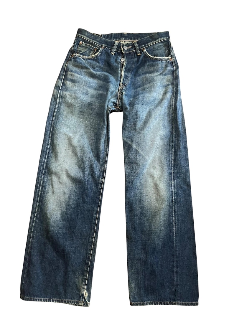 May include: Faded blue denim jeans with a button fly and classic five-pocket design. The jeans show signs of wear and fading, with a slightly relaxed fit. The denim has a vintage look.