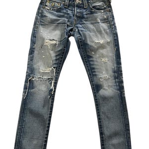 May include: Faded blue denim jeans with distressed details, including rips and worn patches. The jeans have a classic five-pocket design, a button and zipper closure, and a straight leg fit. The jeans are a medium wash with subtle fading.