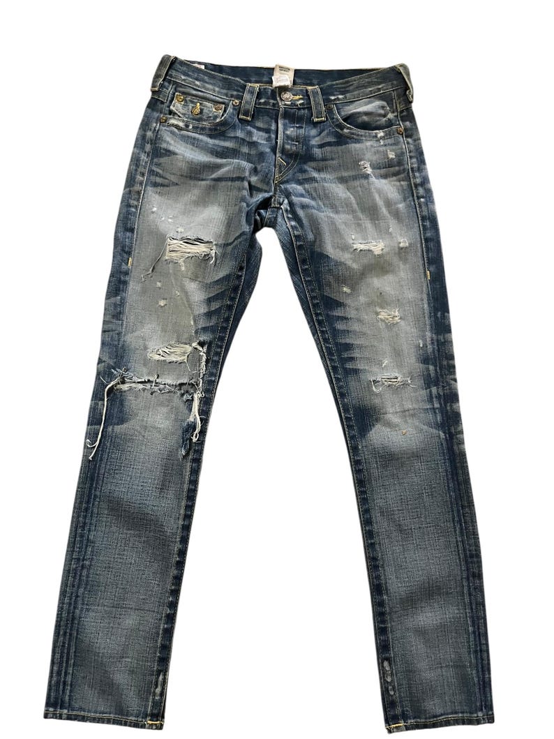 May include: Faded blue denim jeans with distressed details, including rips and worn patches. The jeans have a classic five-pocket design, a button and zipper closure, and a straight leg fit. The jeans are a medium wash with subtle fading.