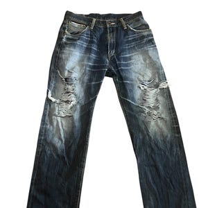 May include: Dark wash denim jeans with distressed details. The jeans have multiple rips and tears across the front of the legs. The denim has a faded, worn appearance.