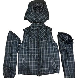May include: A black and white plaid puffer jacket with detachable sleeves and a detachable hood. The jacket features a central black zipper, two front pockets, and a high collar. The sleeves and hood are separated from the main body of the jacket.
