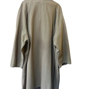 May include: A light olive green coat with a wide collar and long sleeves. The coat has a relaxed fit and a simple design, suitable for layering. The back view shows the coat's full length and construction.