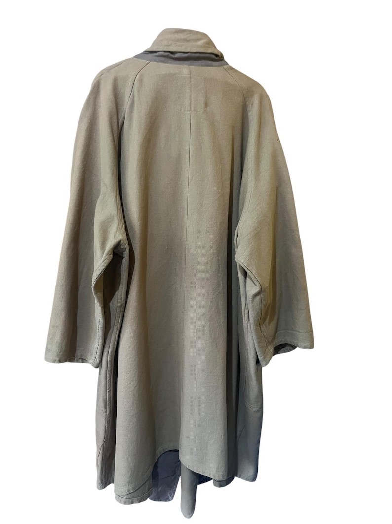 May include: A light olive green coat with a wide collar and long sleeves. The coat has a relaxed fit and a simple design, suitable for layering. The back view shows the coat's full length and construction.