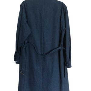 May include: A dark navy blue coat with a matching belt. The coat is hanging on a black hanger. The coat has long sleeves and a collar.