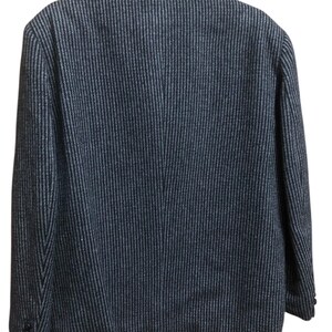 May include: Back view of a dark blue blazer with a subtle vertical stripe pattern. The blazer has a classic design with a notched collar and buttoned cuffs. The fabric appears to be a textured weave, suitable for cooler weather.