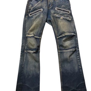 Könnte beinhalten: Verblasste blaue Jeans mit mehreren Reißverschlusstaschen und dekorativen Nähten. Die Jeans haben einen Used-Look mit verblichenen Bereichen und einem klassischen Fünf-Taschen-Design. Die Knie haben ein einzigartiges Designelement.