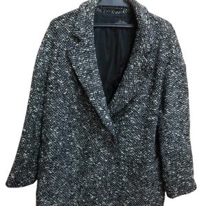 May include: A black and white speckled coat hanging on a black hanger. The coat has a wide lapel and a black lining. The fabric has a textured appearance.