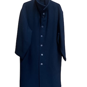 May include: A long, dark navy coat with a high collar and button-down front. The coat is hanging on a black hanger. The coat appears to be made of a heavy fabric, suitable for cold weather.