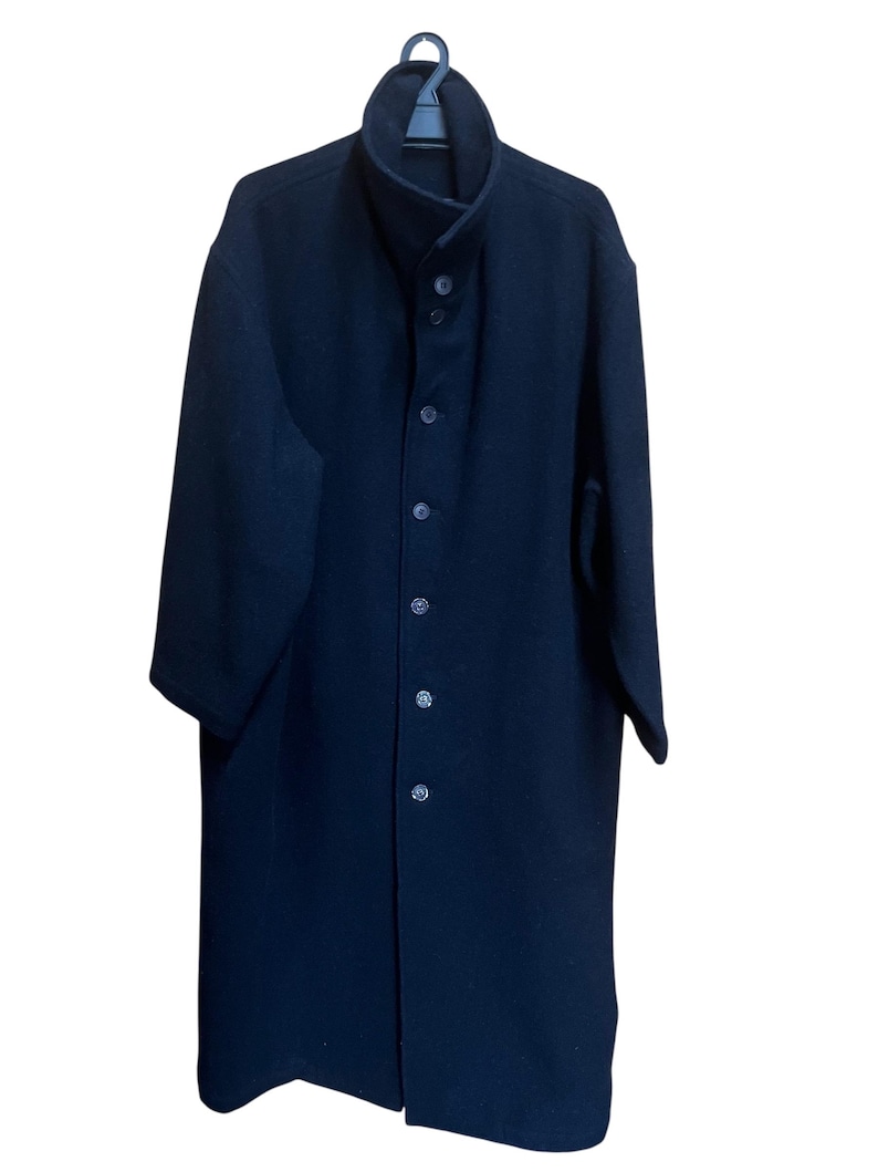 May include: A long, dark navy coat with a high collar and button-down front. The coat is hanging on a black hanger. The coat appears to be made of a heavy fabric, suitable for cold weather.