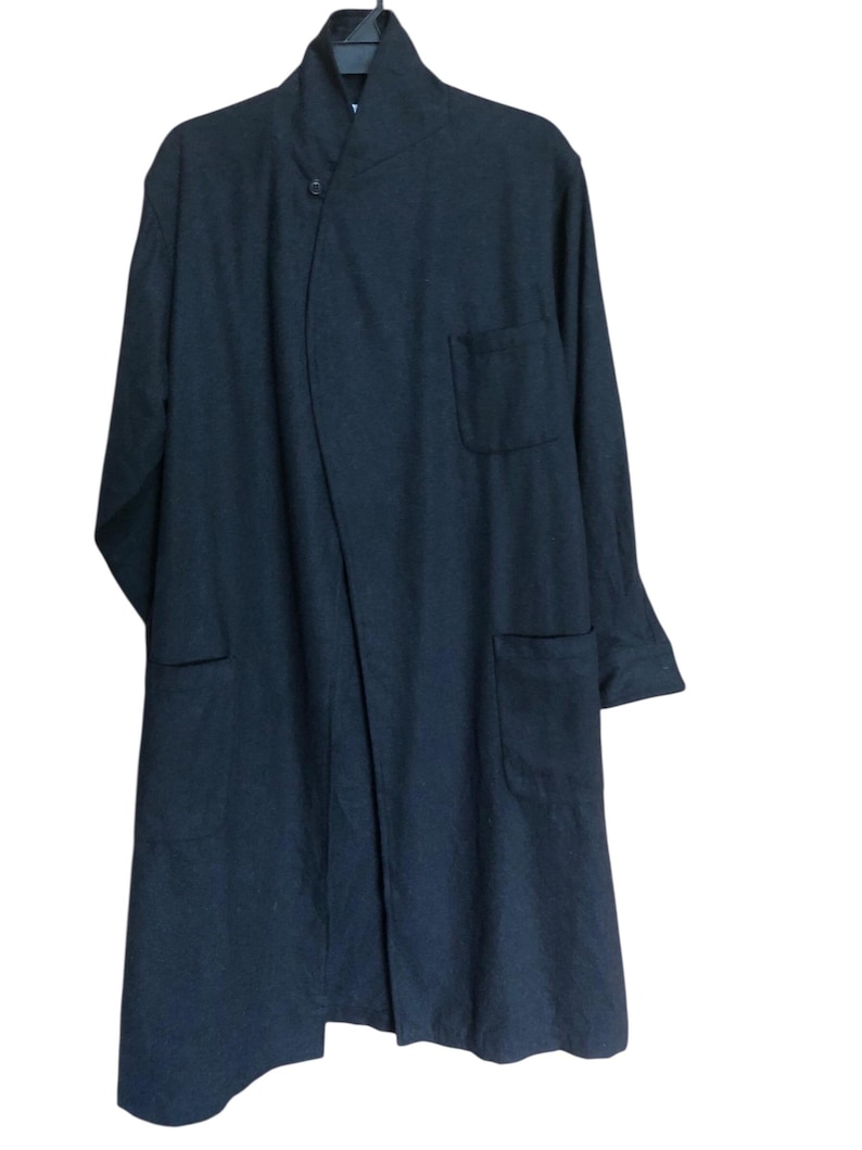 May include: A dark navy blue long coat with a unique asymmetrical design. The coat features a mandarin collar, a single button closure, and two front pockets. The fabric appears to be a soft, woven material.