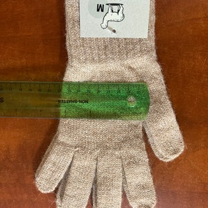 May include: A pair of beige alpaca gloves with a size M tag attached. The tag reads "Mother Nature's Finest Fiber USA Alpaca Made in the USA with U.S. Grown Alpaca".
