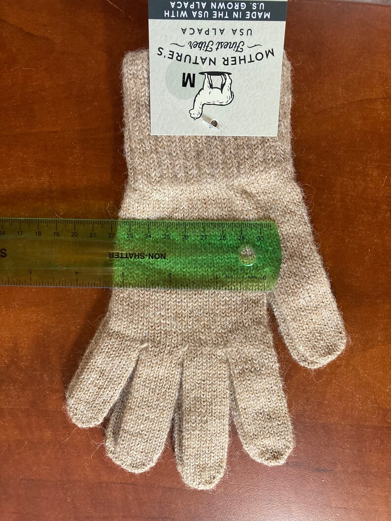 May include: A pair of beige alpaca gloves with a size M tag attached. The tag reads "Mother Nature's Finest Fiber USA Alpaca Made in the USA with U.S. Grown Alpaca".