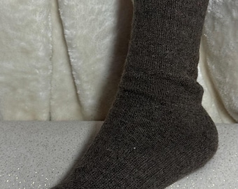 May include: A single brown sock made of a ribbed knit fabric. The sock is displayed upright, showcasing the heel and toe. The background is a soft, white, textured fabric.