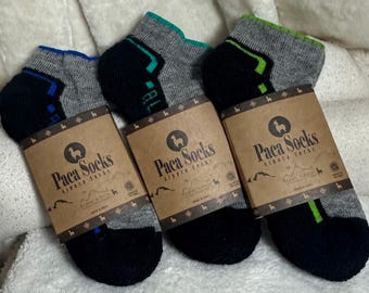 May include: Three pairs of grey, black, and blue ankle socks with the text "Paca Socks" on the packaging. The socks have accents of blue, green, and black. The socks are made of alpaca fibre.