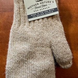 K&ouml;nnte beinhalten: Ein Paar beigefarbene Alpaka-Handschuhe mit einem Etikett mit der Aufschrift "Mother Nature's Finest Fiber - USA Alpaca. Made in the USA with U.S. Grown Alpaca". Das Etikett zeigt eine kleine Alpaka-Illustration und die Gr&ouml;&szlig;e "S".