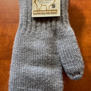 K&ouml;nnte beinhalten: Graue Alpaka-Wollhandschuhe mit einem braunen Etikett mit der Aufschrift "Mother Nature's Finest Fiber" und "Made with Pride in the U.S.A. by the N.E. Alpaca Fiber Pool Inc."