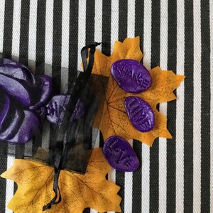 May include: Three purple, glittery, resin stones with the words "Change", "Time", and "Love" on them. The stones are on a yellow leaf with black and white stripes in the background.