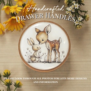 Op de afbeelding: Ronde ladeknop met een licht houten frame. Het midden heeft een aquarel illustratie van een hert en een konijn. Het hert is bruin met witte vlekken en het konijn is lichtbruin. Tekst: "Handcrafted DRAWER HANDLES".