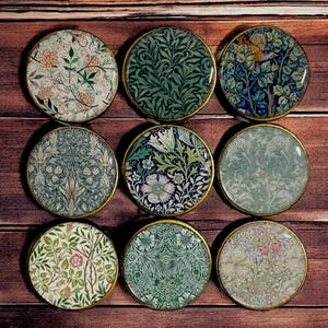 May include: Nine round, decorative, floral patterned coasters with gold trim. The coasters feature a variety of floral and leaf designs in shades of green, blue, white, and pink.