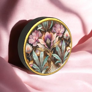 May include: A round wooden box with a gold trim and a floral design. The design features pink, purple, and green flowers on a brown background.