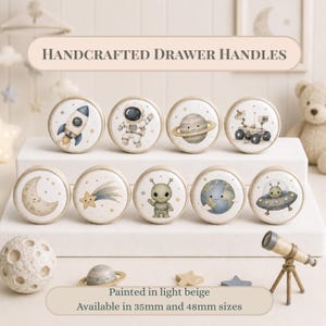May include: Nine round drawer handles featuring watercolour space illustrations including a rocket, astronaut, planet, rover, moon, shooting star, alien, Earth, and UFO. Text reads: HANDCRAFTED DRAWER HANDLES. Painted in light beige. Available in 35mm and 48mm sizes.