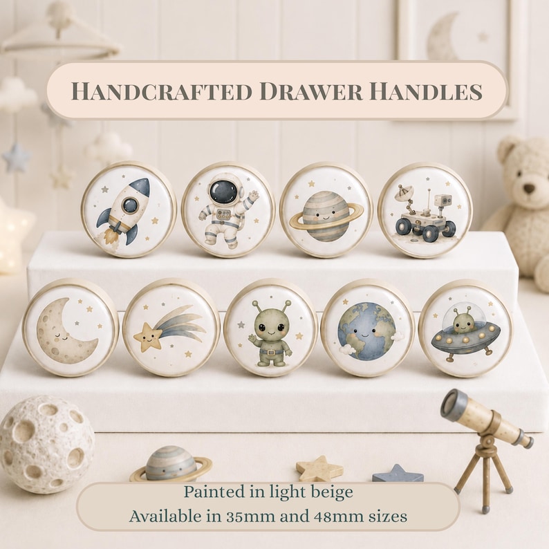 May include: Nine round drawer handles featuring watercolor space illustrations including a rocket, astronaut, planet, rover, moon, shooting star, alien, Earth, and UFO. Text reads: HANDCRAFTED DRAWER HANDLES. Painted in light beige. Available in 35mm and 48mm sizes.
