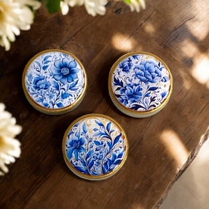 May include: Three round decorative coasters with a blue and gold floral design. The coasters are made of wood and have a glossy finish.