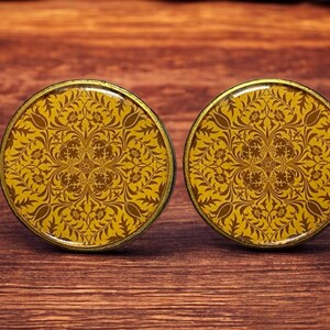Könnte beinhalten: Ein Paar runde, goldfarbene Manschettenknöpfe mit einem gelben und braunen Blumenmuster.
