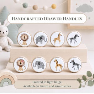 May include: Eight round wooden drawer handles featuring illustrations of a lion, elephant, giraffe, and zebra. The text reads Handcrafted Drawer Handles, Painted in light beige, Available in 35mm and 48mm sizes. The handles are arranged on two levels.