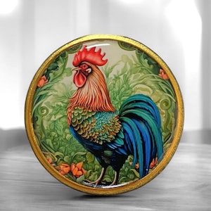 May include: A round, gold-rimmed knob with a colorful rooster illustration. The rooster has a red comb and wattle, green and blue feathers, and is standing in a green and white floral pattern.