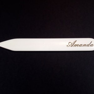 May include: White paper letter opener with a pointed tip and the name "Amanda" engraved on the surface.