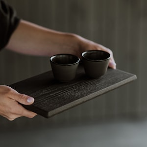 May include: A black wooden serving tray with two small black ceramic cups on top.