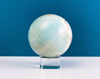 May include: A light blue and white agate sphere on a clear glass pedestal. The sphere is smooth and polished.