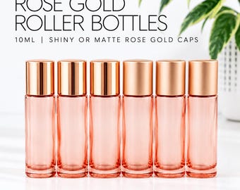 May include: Six 10ml glass roller bottles with rose gold caps. The text reads ROSE GOLD ROLLER BOTTLES 10ML | SHINY OR MATTE ROSE GOLD CAPS. The bottles are clear with a light pink tint, featuring a cylindrical shape and metallic finish caps.