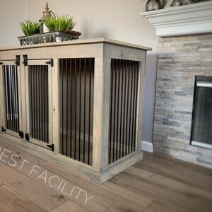 May include: A light wood dog crate with two doors and black metal bars. The crate is sitting on a wood floor in front of a fireplace.