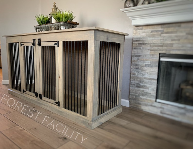 May include: A light wood dog crate with two doors and black metal bars. The crate is sitting on a wood floor in front of a fireplace.