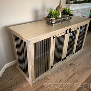 May include: A light wood dog crate with two doors and a top surface. The crate has black metal bars and black metal hinges. The top surface has a decorative tray with a small potted plant.
