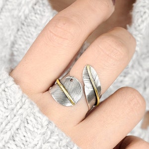 May include: A silver and gold feather ring with a delicate design. The ring is adjustable and can be worn on any finger.