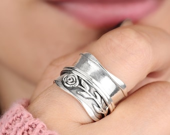 May include: A silver spinning ring with a floral design. The ring is worn on a person's finger.