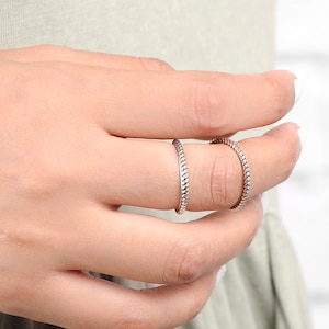 May include: Two silver rings with a braided design worn on a finger.