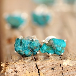 May include: A pair of silver earrings with turquoise stones. The stones are a deep blue-green colour and have a rough, natural texture.
