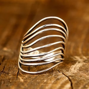 May include: A silver ring with a wavy, open design. The ring is made of multiple thin bands of metal that are woven together.