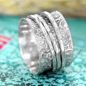 Puede incluir: Un anillo giratorio de plata con un dise&ntilde;o floral texturizado. El anillo tiene tres bandas que giran libremente.